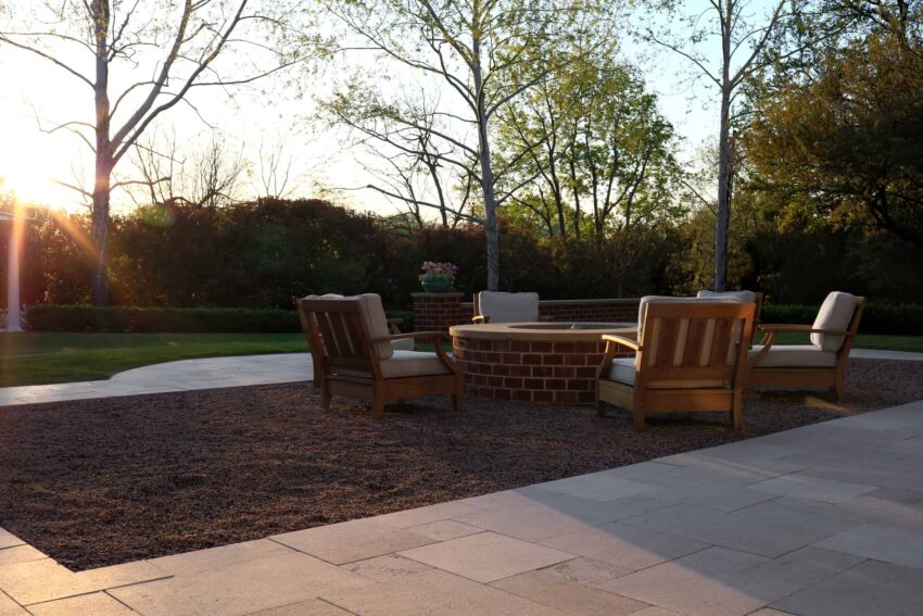 Brick firepit with limestone coping and teak restoration hardware chairs in gravel area